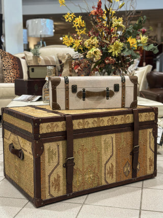 Two vintage-style trunks on a tiled floor with a floral arrangement in the background.