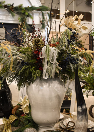 Decorative Christmas flower arrangement with greenery, ribbons, and berries in a white vase.