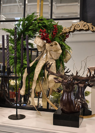 Decorative arrangement with a wreath, candles, and a deer sculpture in a room setting.