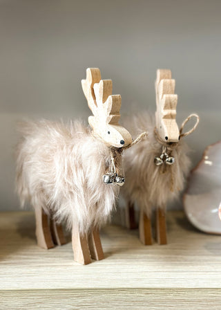 Two wooden reindeer figurines with fluffy white fur on a wooden surface.