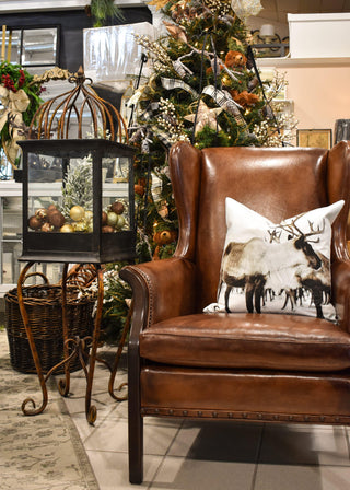 Brown leather armchair with a decorative pillow featuring reindeer, in front of a Christmas tree.